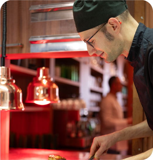 Chef en pleine préparation d’un plat en cuisine, concentré sous une lumière chaleureuse.