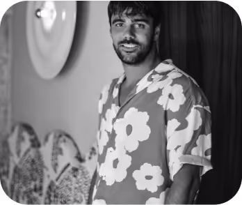 Un homme portant une chemise à motifs floraux, souriant devant un mur à la décoration artistique du restaurant.